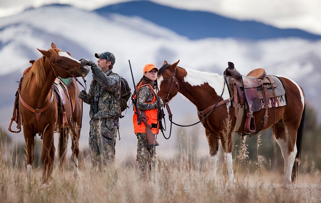 Male and female hunter with horses in wilderness