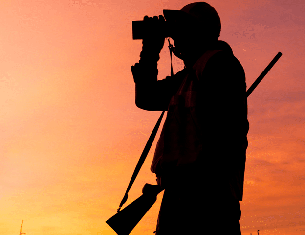 Silhouette of hunter with binoculars at dawn